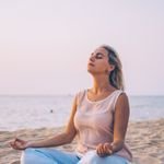 Meditating woman practicing mindfulness on a tranquil beach at sunset, promoting relaxation and wellness.