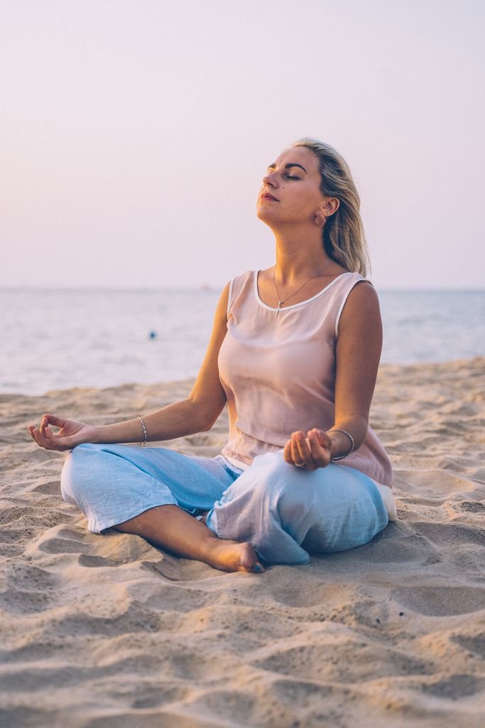 Meditating woman practicing mindfulness on a tranquil beach at sunset, promoting relaxation and wellness.